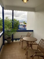 A balcony with a table and chairs, a potted plant, and a view of the sea and a red boat.