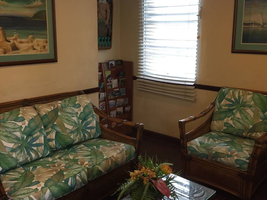 A room with a wooden sofa and armchairs, a coffee table with a floral vase, and a window with blinds.