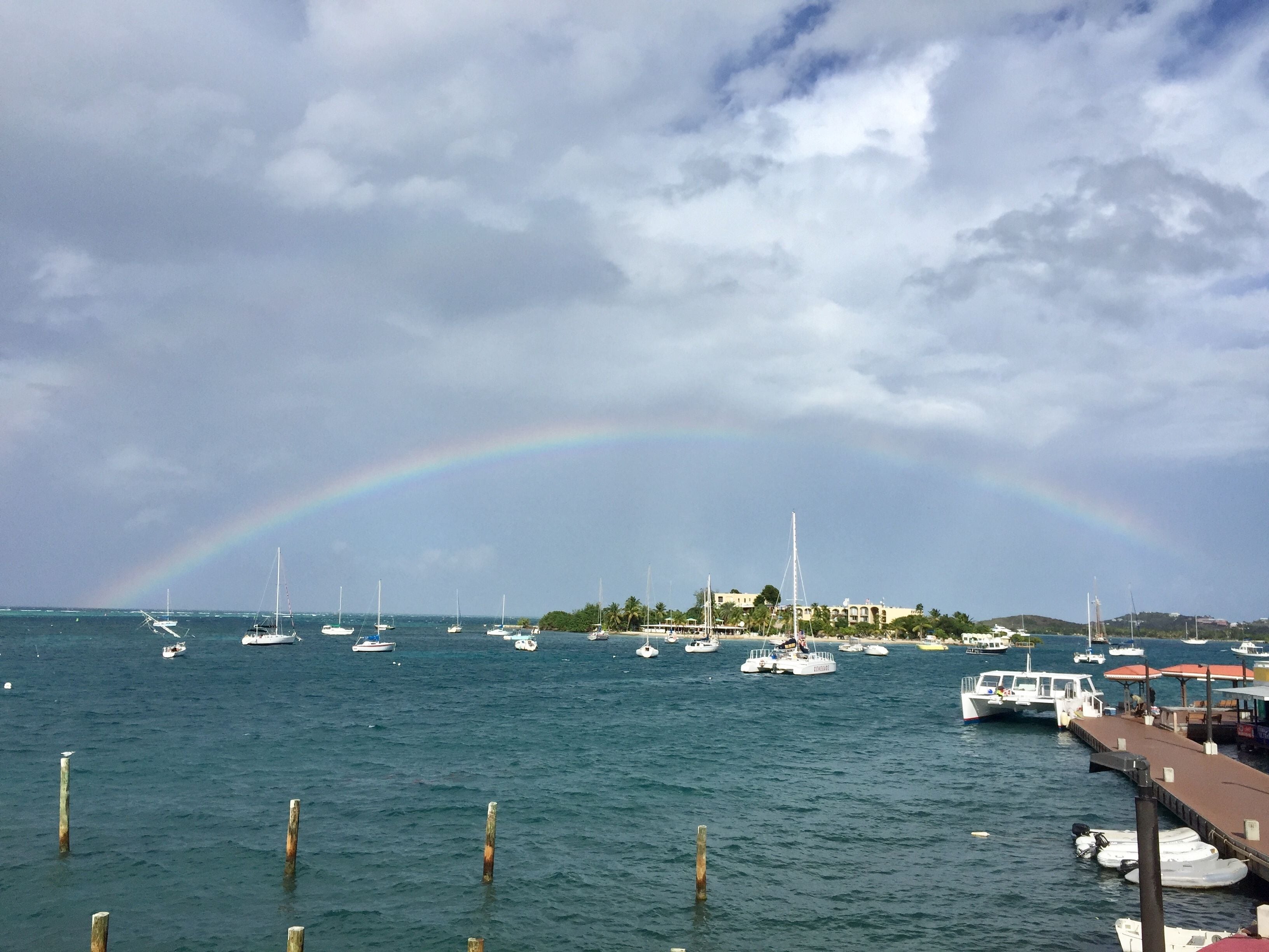Un port de plaisance avec des bateaux amarrés, une jetée et un arc-en-ciel dans le ciel.