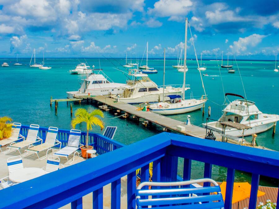 A marina with several boats docked, a pier with lounge chairs, and a clear blue sky.