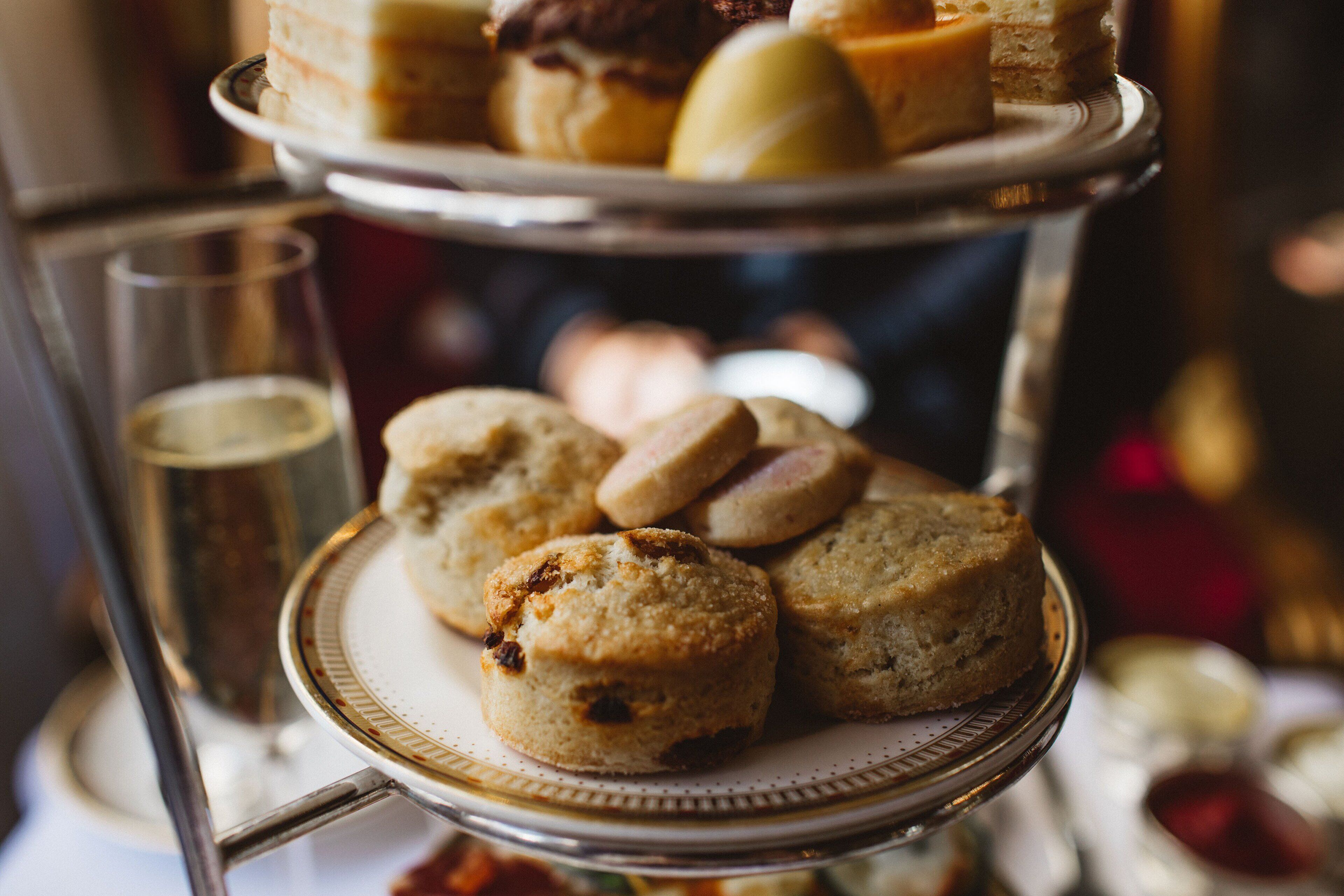 Un présentoir à étages garni de diverses pâtisseries et un verre d’une boisson de couleur claire.