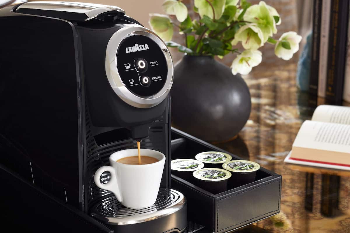 A coffee machine with a cup of coffee and four coffee cups on a tray.