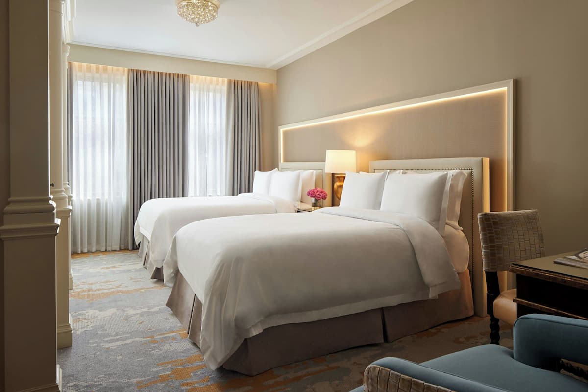 A hotel room with two beds, a desk, and a chair.