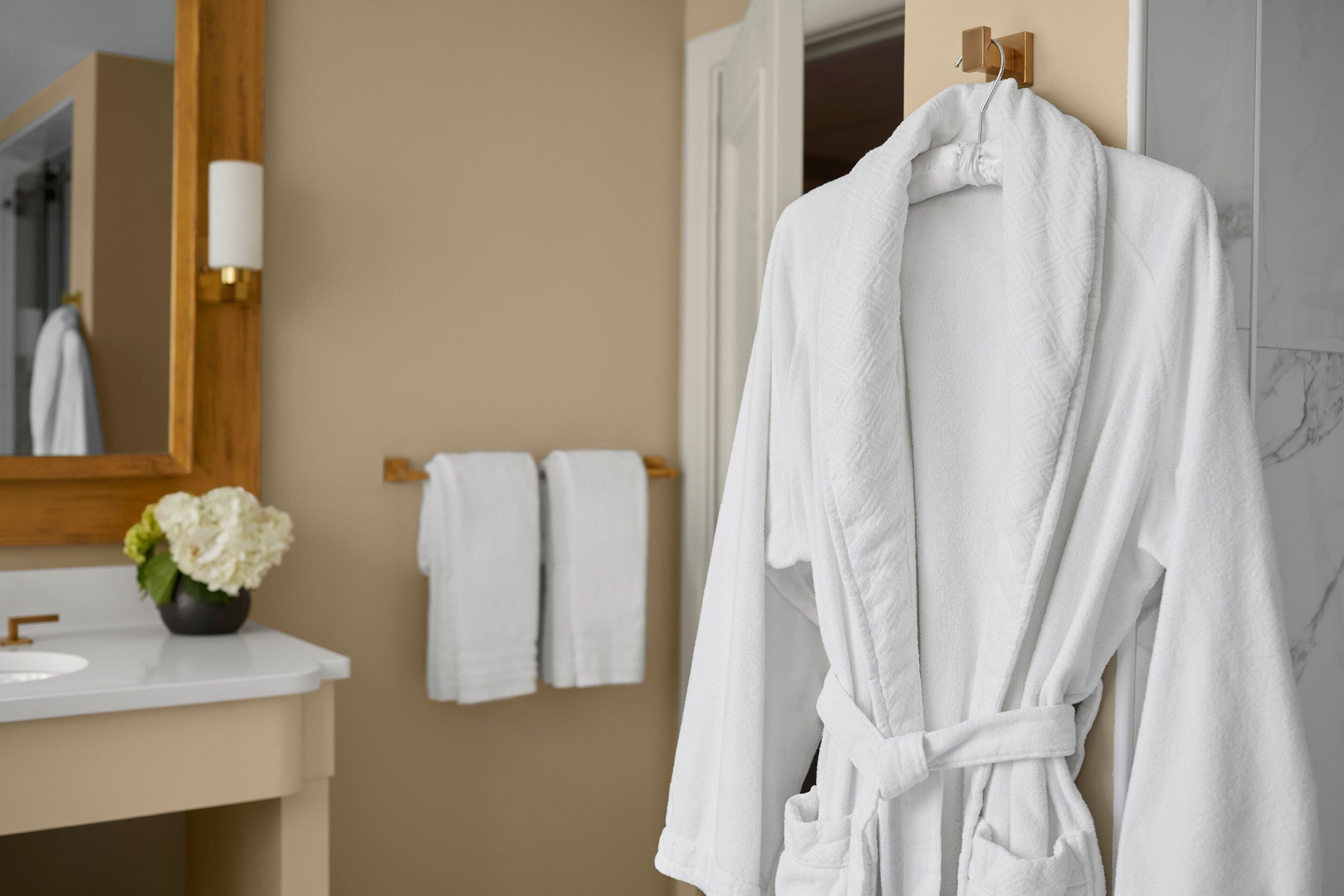 Un baño con una bañera blanca, un perchero de madera y un florero con flores blancas en el tocador.