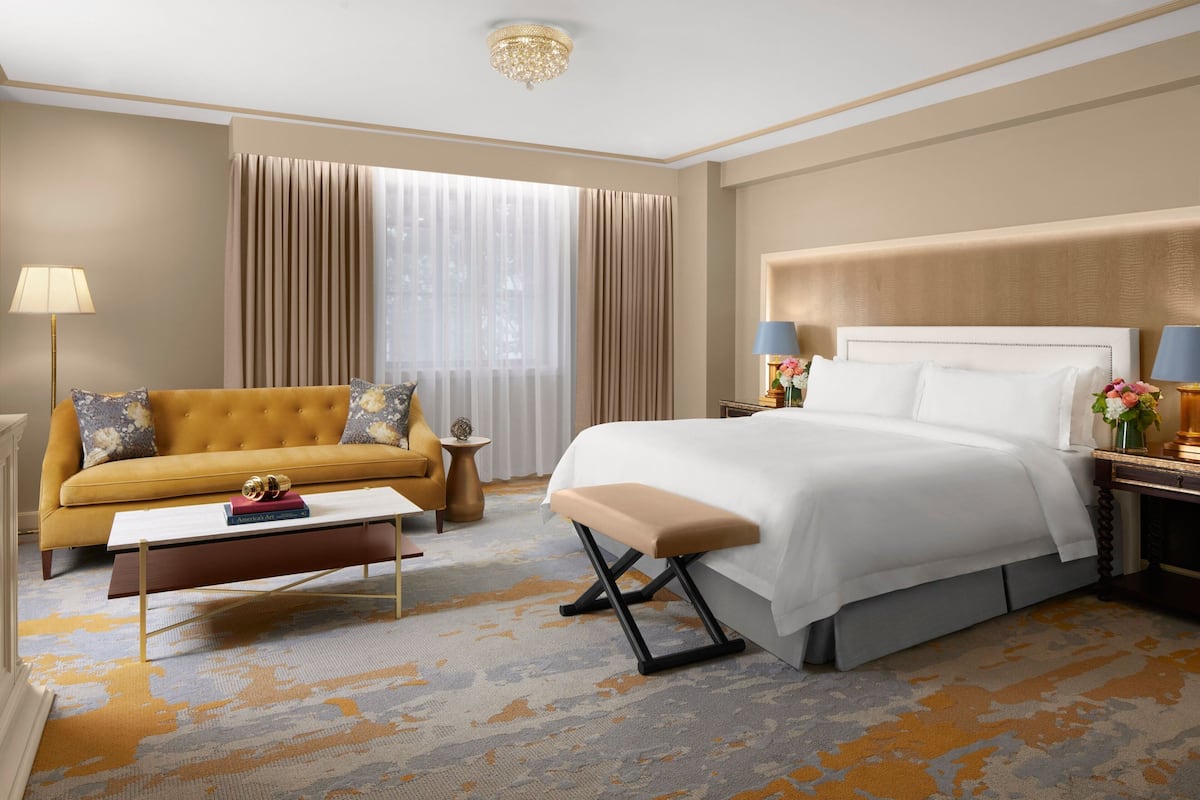 A hotel room with a large bed, a sofa, a coffee table, and a nightstand with lamps.