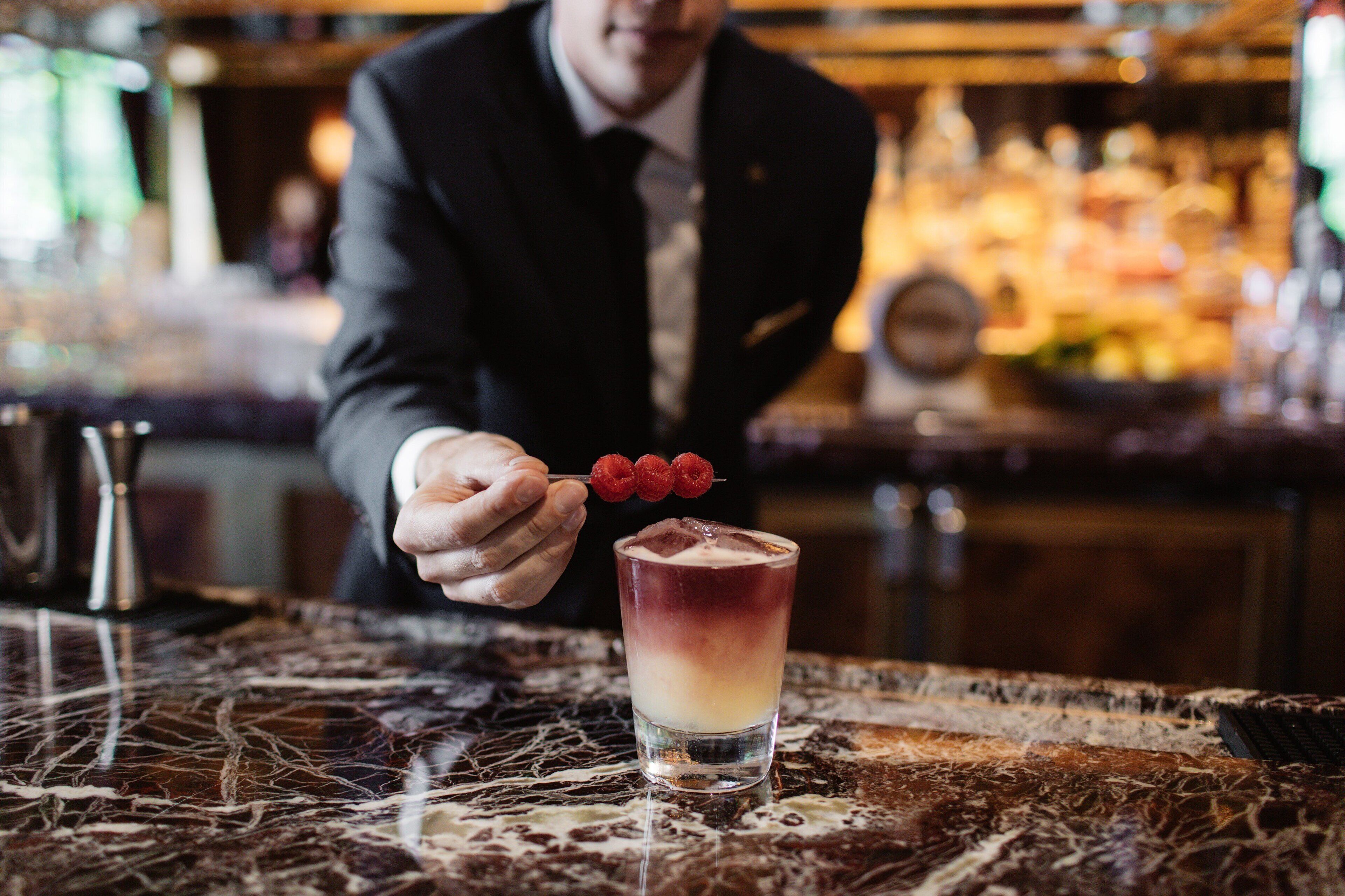 Un barista prepara un cocktail composto, guarnito con un lampone.