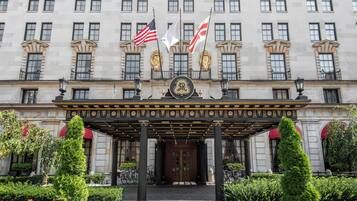 A grand building with a central entrance, flags, and a well-maintained garden.