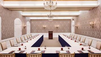 A conference room with a long table, chairs, a podium, and chandeliers.