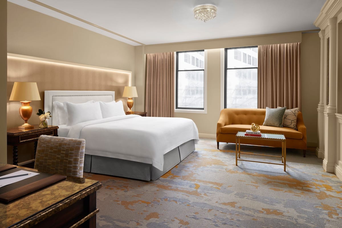 A hotel room with a large bed, a sofa, a coffee table, and a desk.