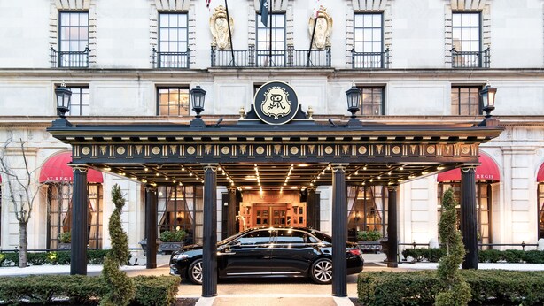 Imponente entrada de hotel con acceso cubierto, columnas y banderas.