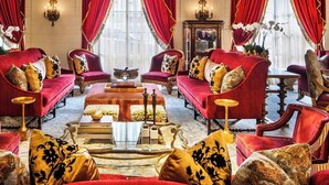Una habitación opulenta con una imponente araña, cortinas rojas y muebles ricamente decorados.