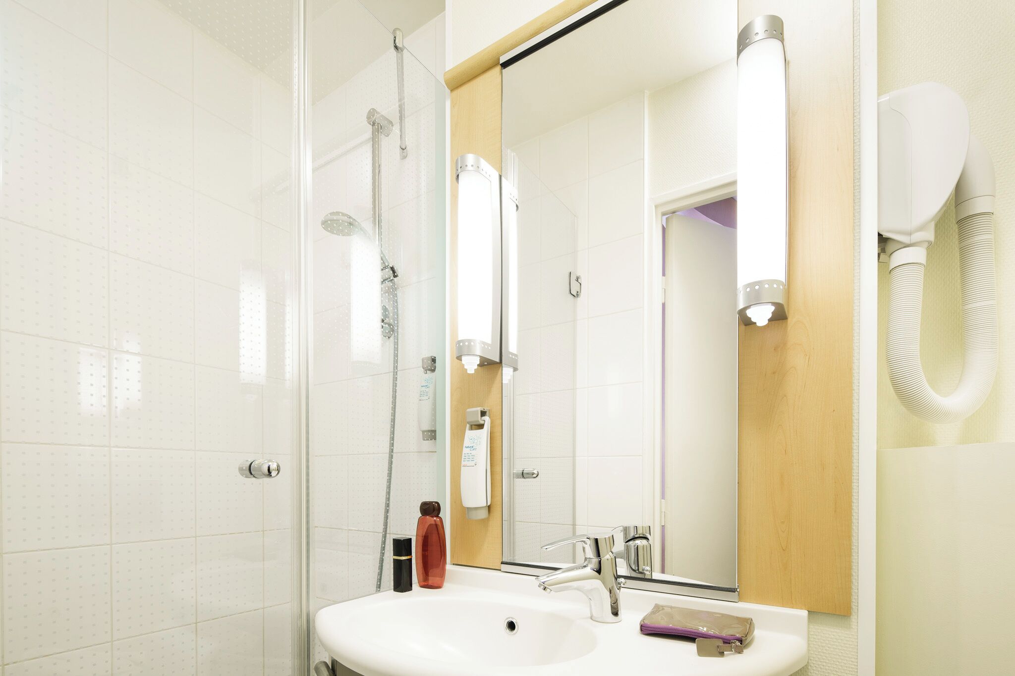 A bathroom with a glass shower enclosure, a sink with a mirror, and a towel dispenser.