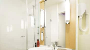 A bathroom with a glass shower enclosure, a sink with a mirror, and a towel dispenser.