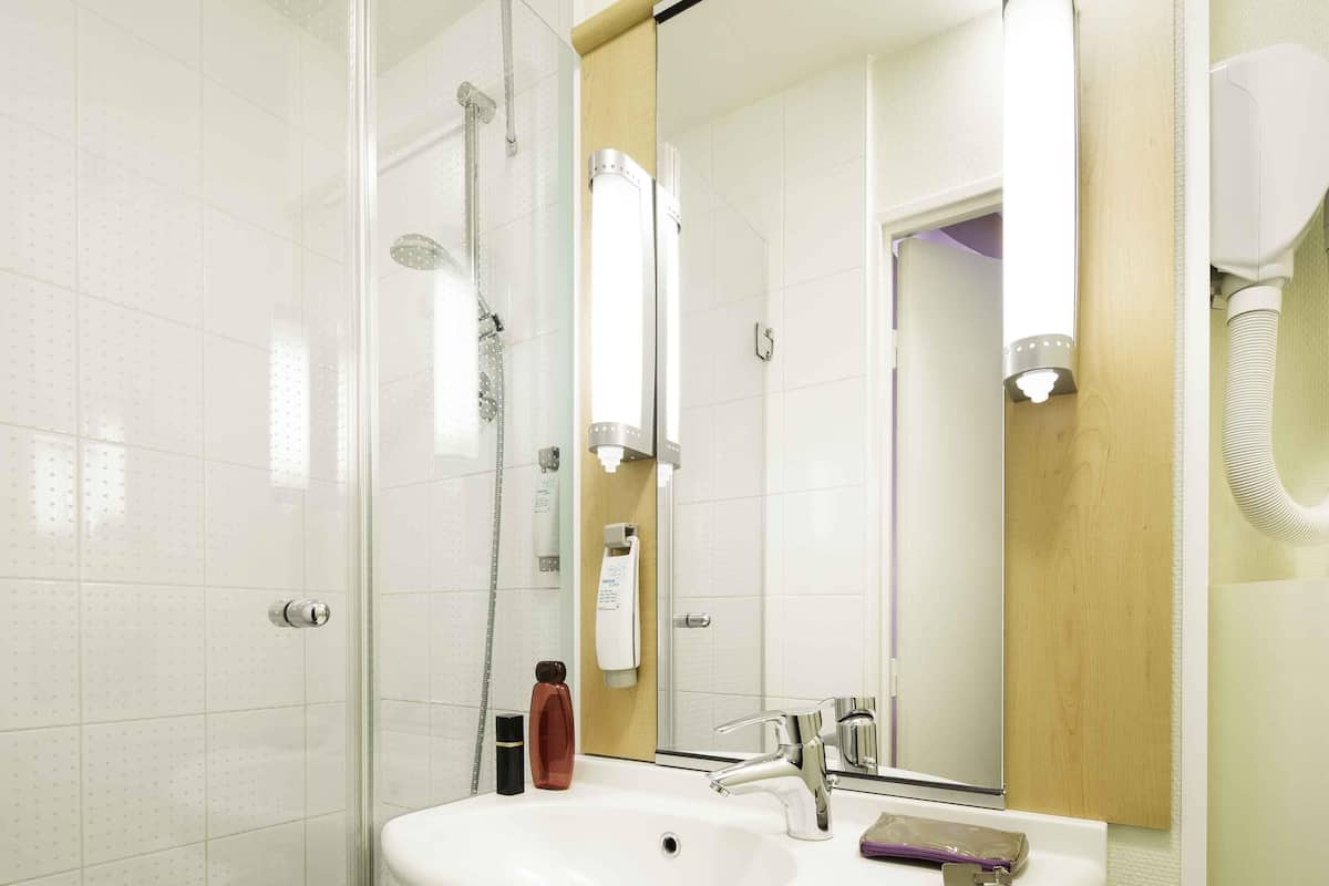 A modern bathroom with a glass shower enclosure, a white sink with a chrome faucet, and a large mirror.