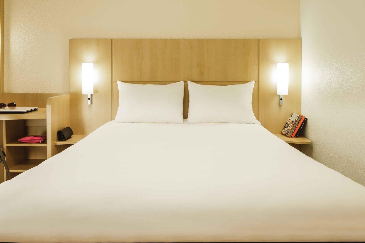 Ein Hotelzimmer mit einem großen Bett, zwei Nachttischen, einem Beistelltisch und einem hölzernen Kopfteil.
