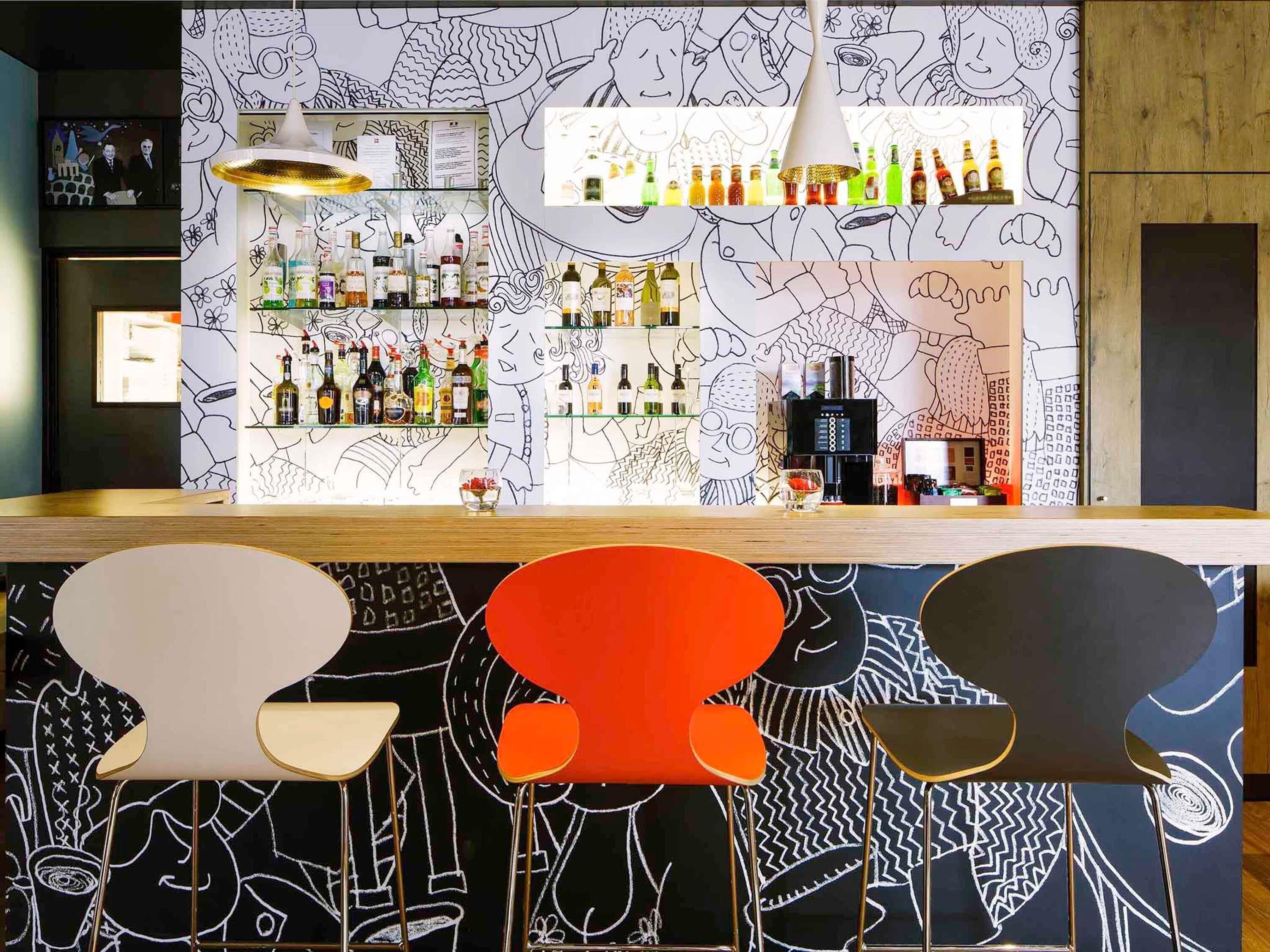 A bar area with a counter, shelves of bottles, and a wall with abstract line drawings.