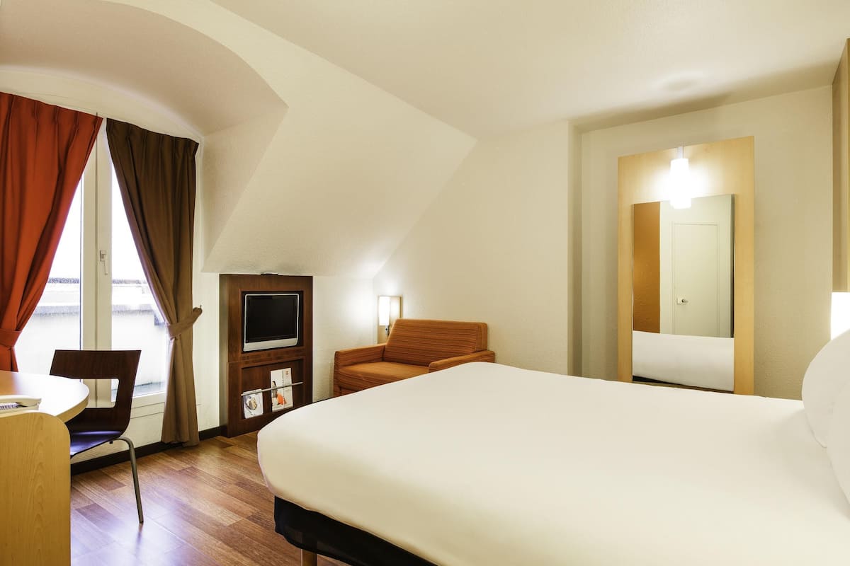 A hotel room with a large bed, a desk with a chair, a television, and a mirror.