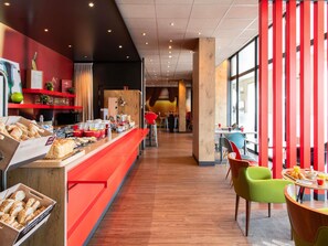 Ein modernes Café mit einer langen Theke, die verschiedene Backwaren und Getränke präsentiert, mit leuchtend roten Akzenten und Blick auf den Gastraum.
