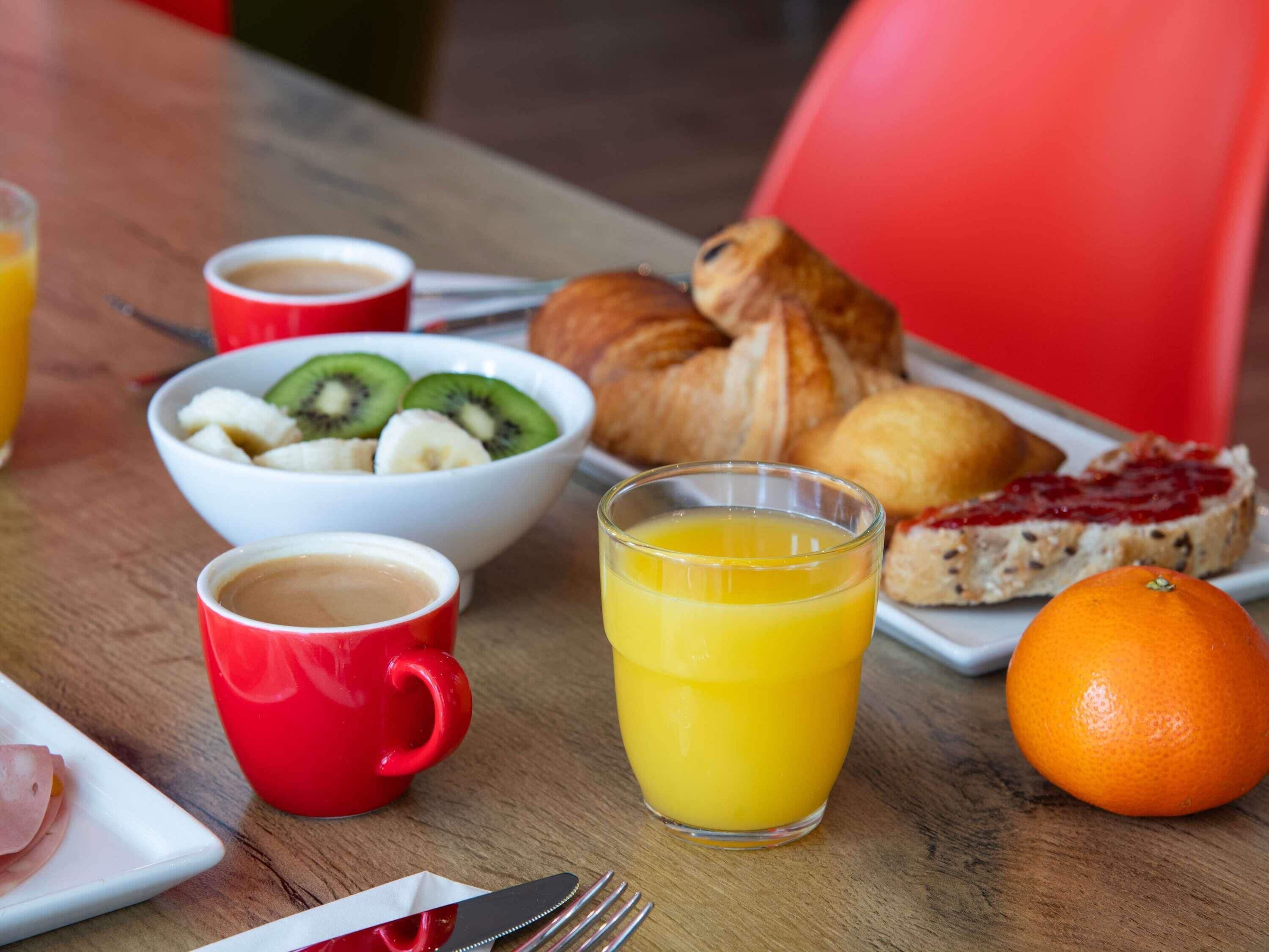 Desayuno con un tazón de fruta, un croissant, jugo de naranja y café.