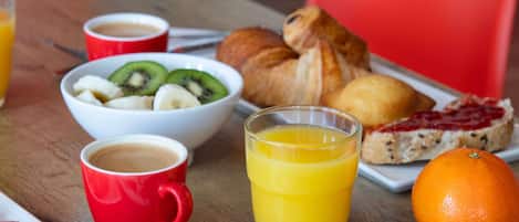 Une table mise pour le petit-déjeuner avec un bol de fruits, un croissant, du jus d’orange et du café.