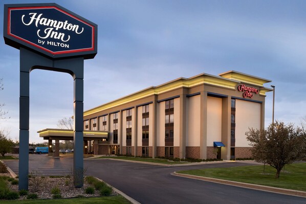 Edifício do Hampton Inn by Hilton com uma grande placa, estacionamento e um gramado bem cuidado.