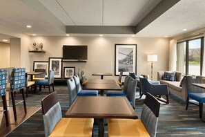 Uma sala de jantar de hotel com várias mesas e cabines, obras de arte nas paredes e uma grande janela com vista para o exterior.