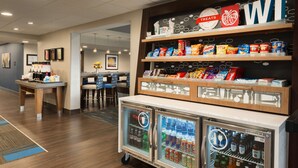 A hotel lobby with a snack bar, a refrigerator with beverages, and a seating area.