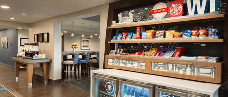 A hotel lobby with a snack bar, a refrigerator with beverages, and a seating area.