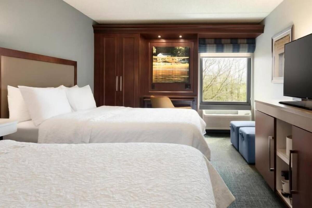 A hotel room with two beds, a TV, a window with a view, and a built-in cabinet.