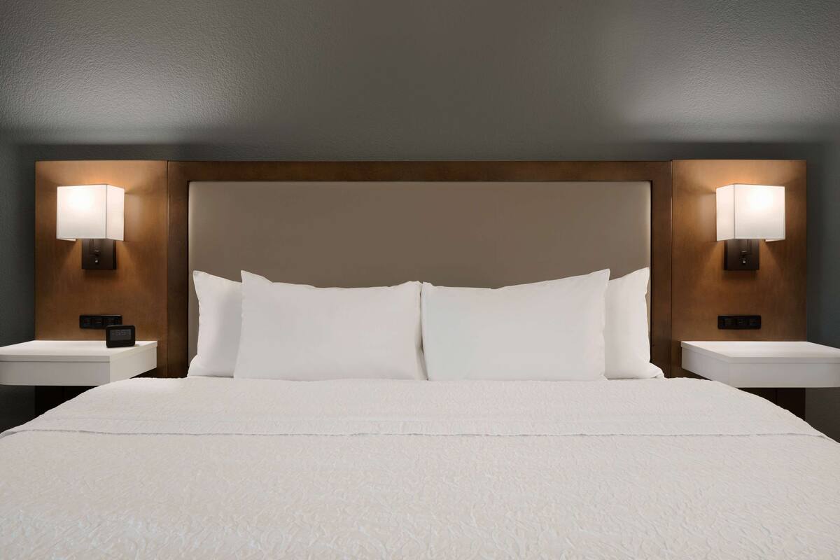 A hotel room with a large bed, two bedside tables, and two wall-mounted lamps.
