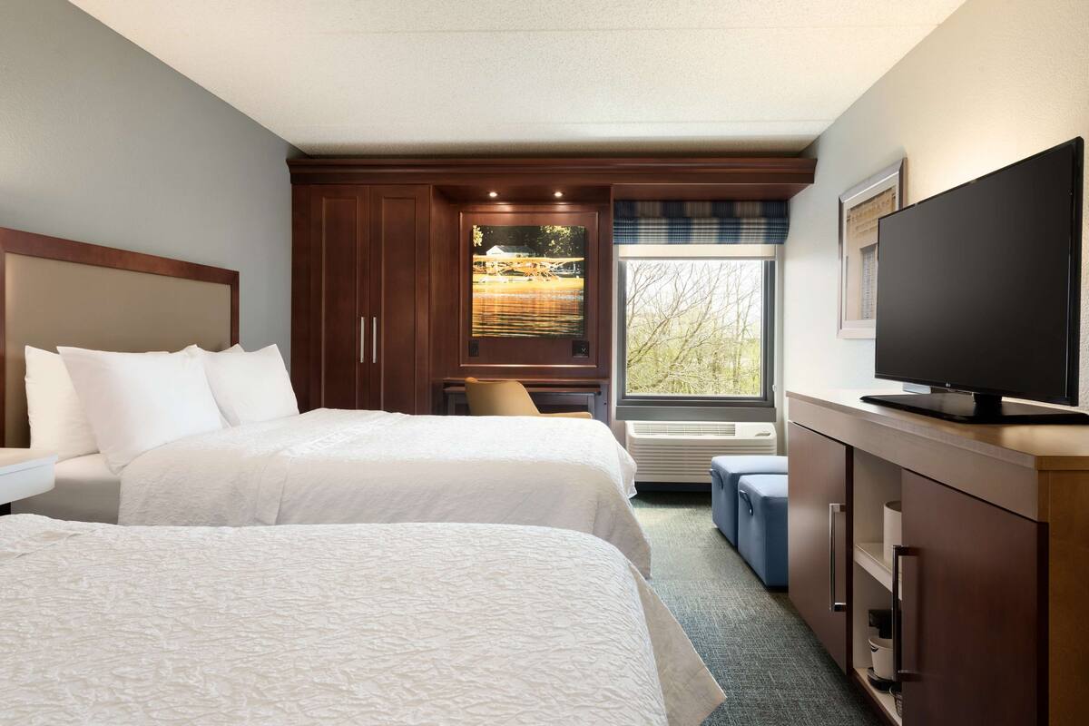 A hotel room with two beds, a television, a window with a view, and a built-in cabinet.
