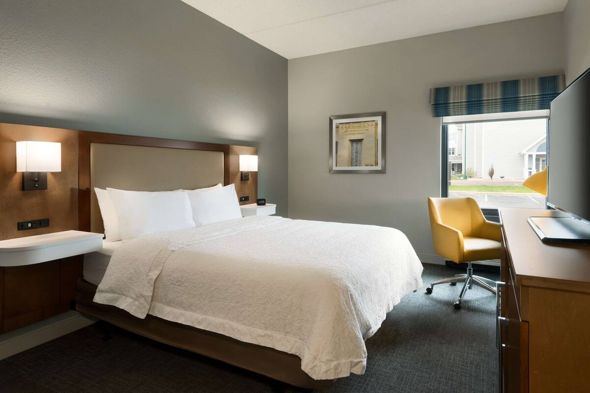 A hotel room with a large bed, bedside lamps, a desk with a chair, and a window with a view of the outside.