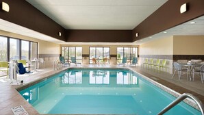 An indoor swimming pool with clear water, surrounded by lounge chairs and tables.