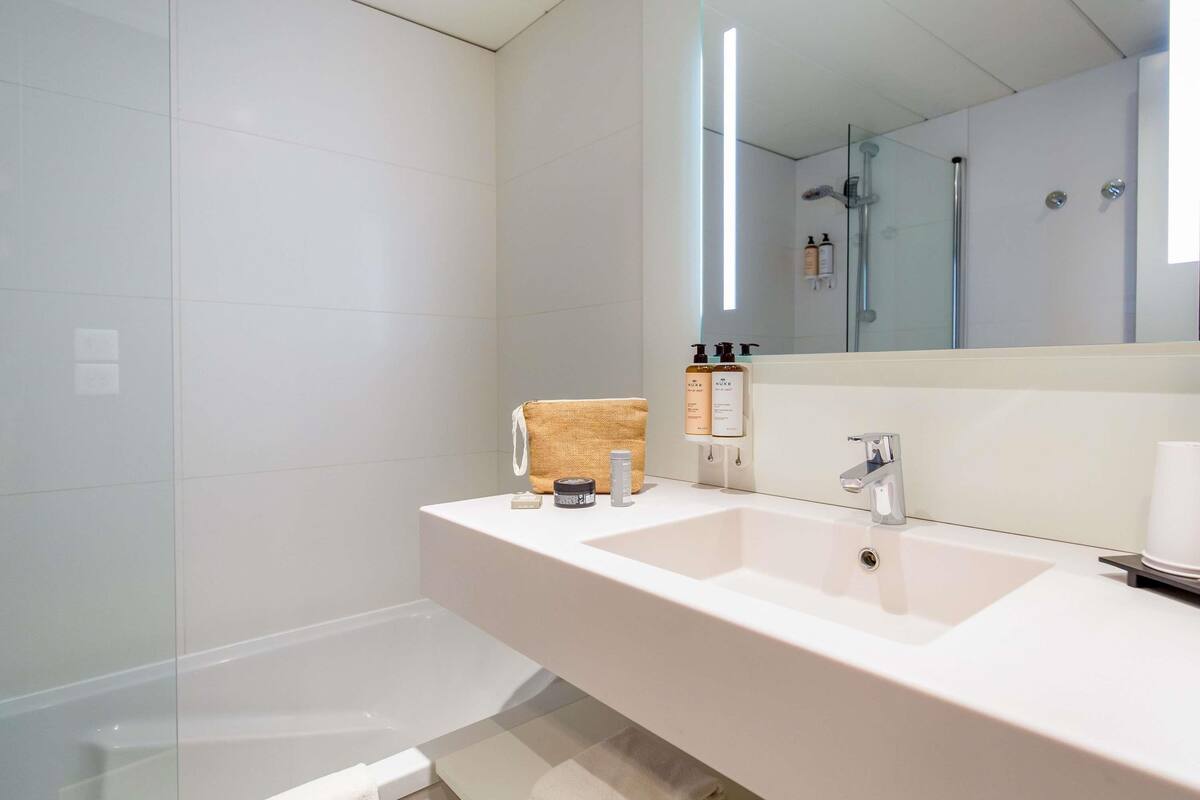 A modern bathroom with a large mirror, two sinks, and a glass shower enclosure.