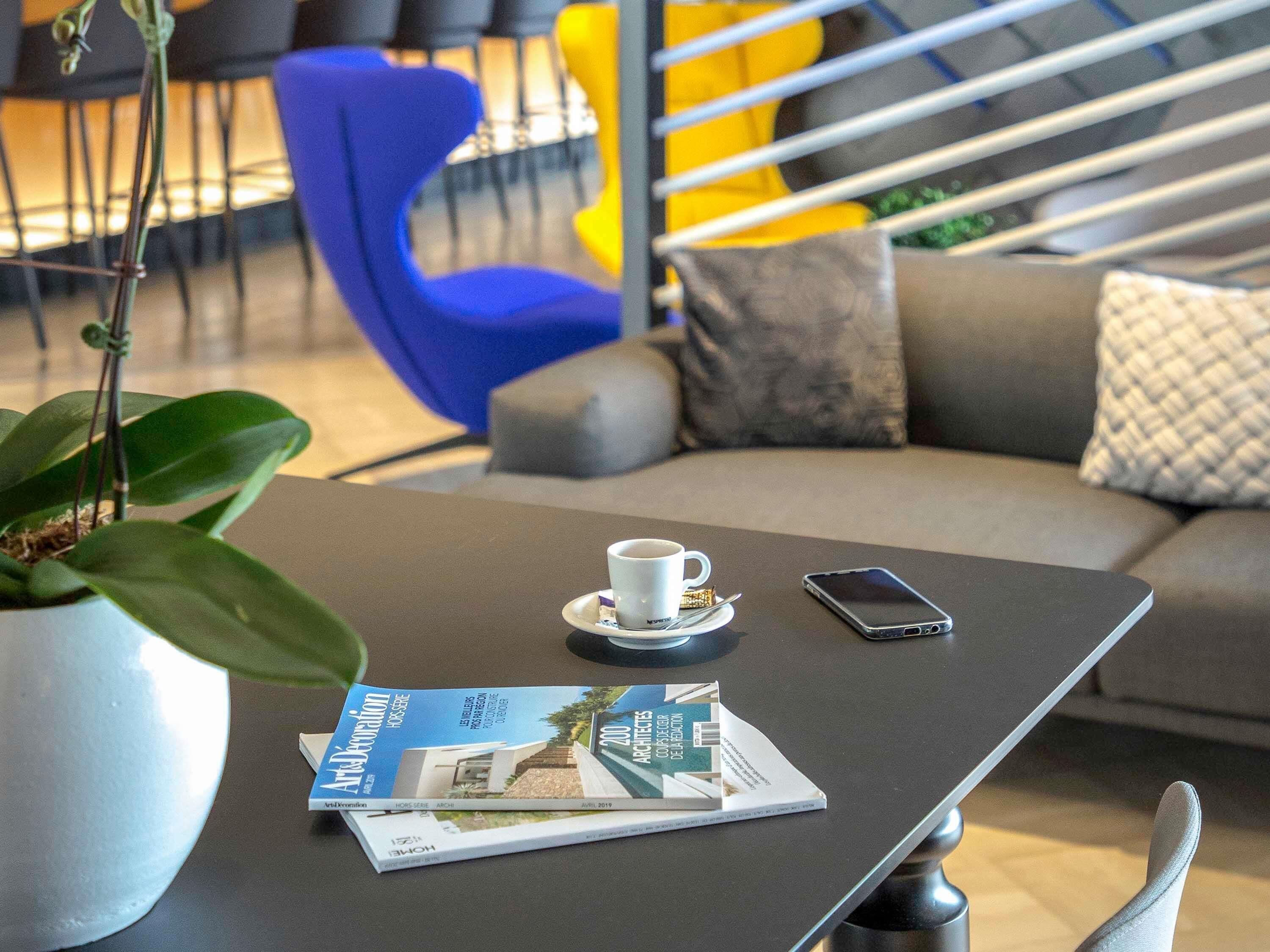 A modern lounge area with a sofa, a coffee table with a magazine, a cup, and a smartphone.