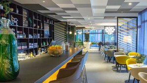 A modern bar area with a checkered ceiling, bar stools, and a seating area with yellow chairs.