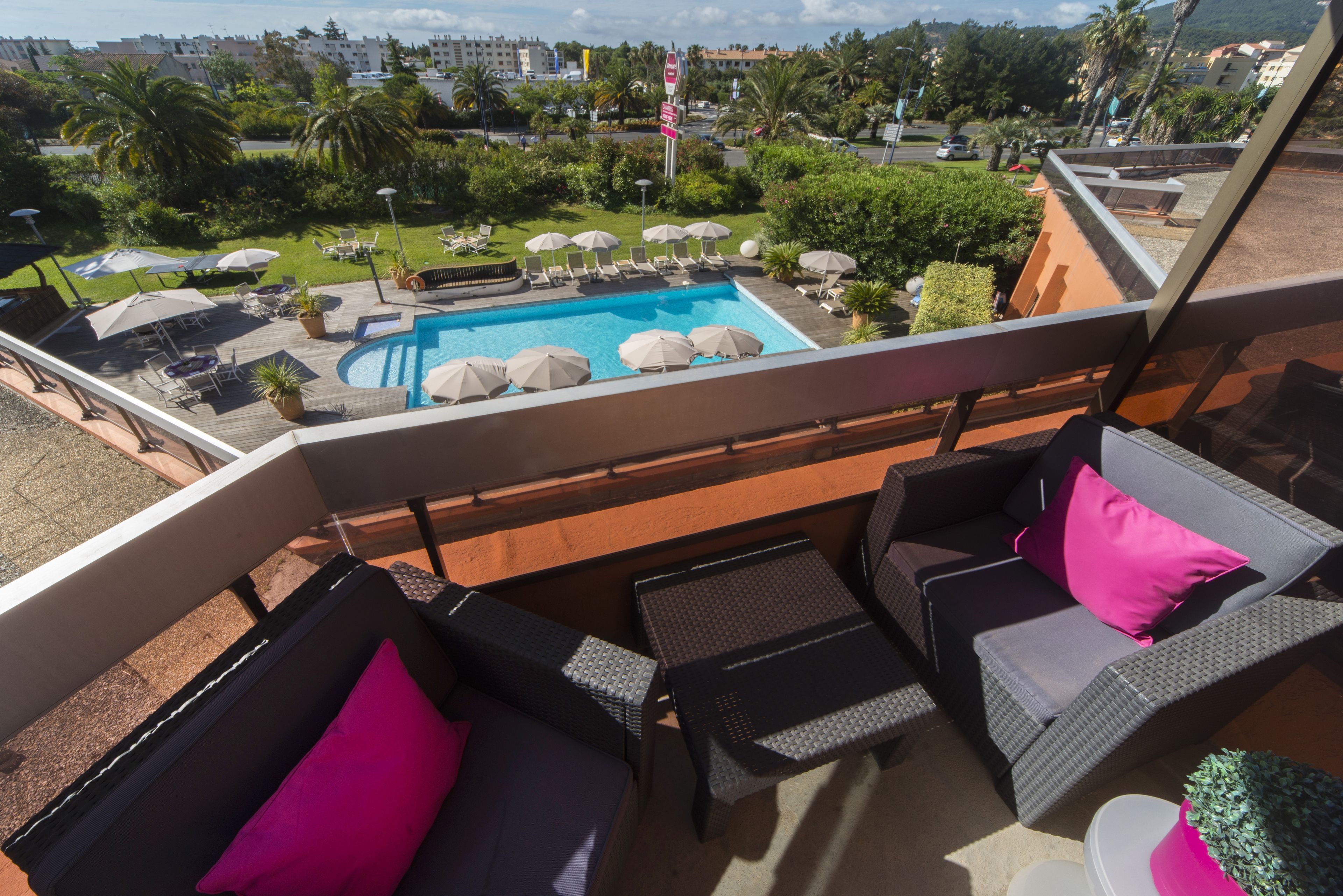 A balcony with wicker furniture, a pool, and a view of the surrounding greenery and buildings.