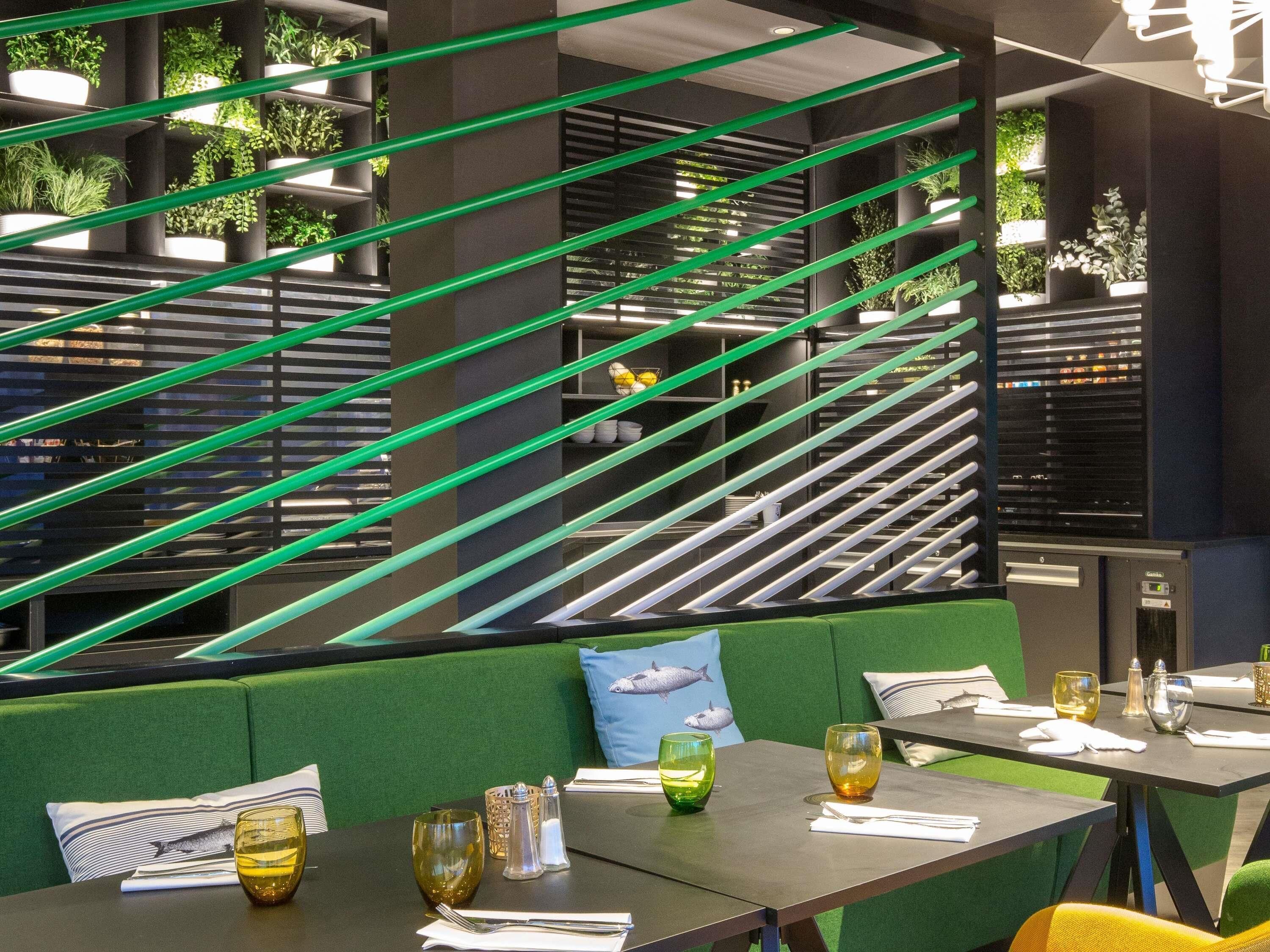 A modern restaurant with green upholstered seating, tables with cutlery, and green-striped partitions.