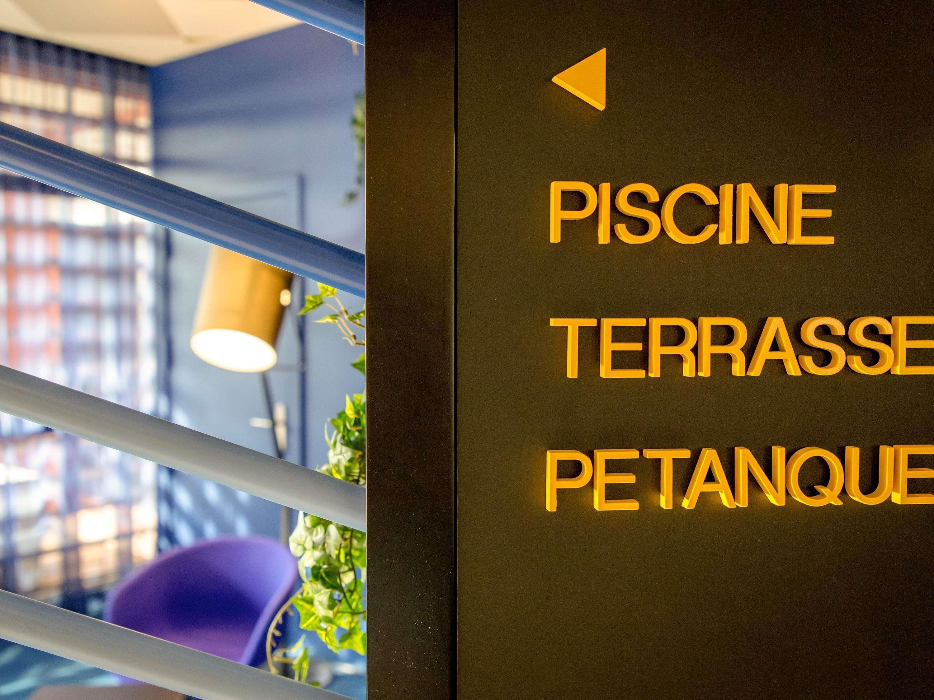 Ein Schild mit Pfeilen und der Aufschrift 'PISCINE TERRASSE PETANQUE', das einen Ort kennzeichnet.
