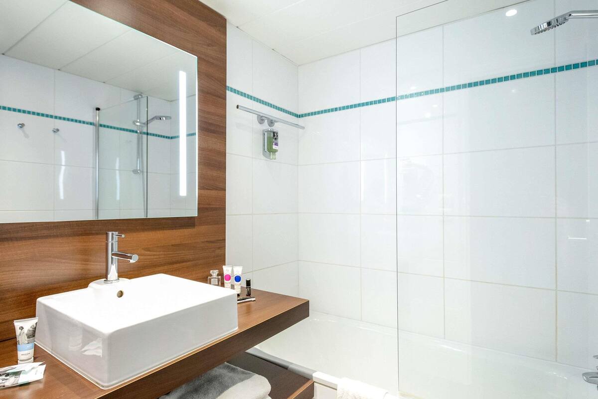 A modern bathroom with a white sink, mirror, and shower.