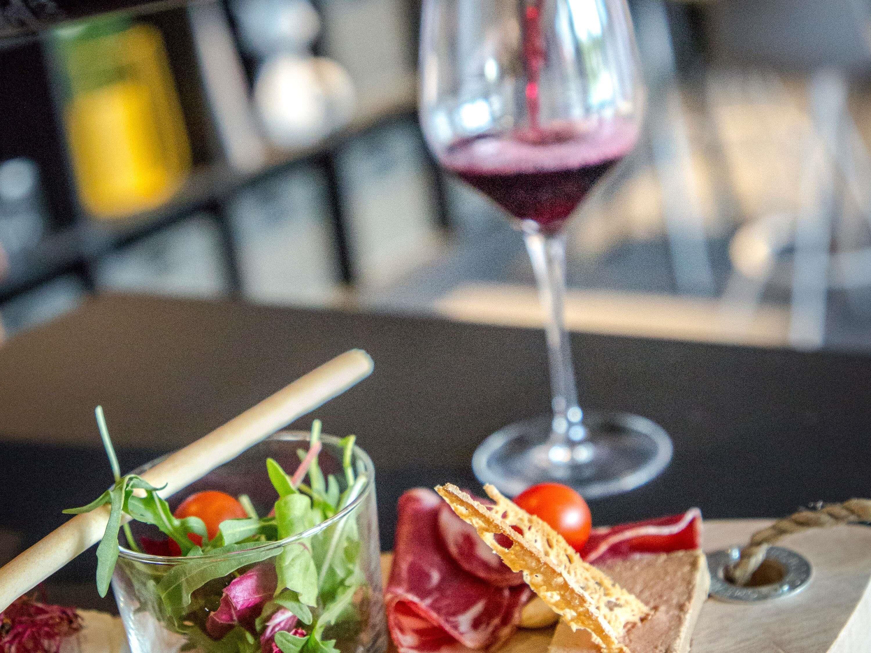 Un verre de vin rouge, une assiette de salade avec une petite fourchette en bois, et un morceau de pain sur une table.