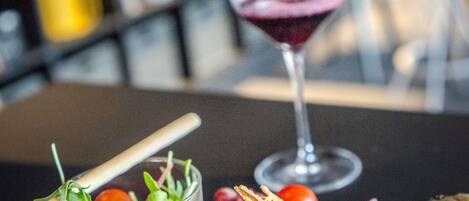 A glass of red wine, a glass of salad with a wooden stick, and a piece of bread on a table.