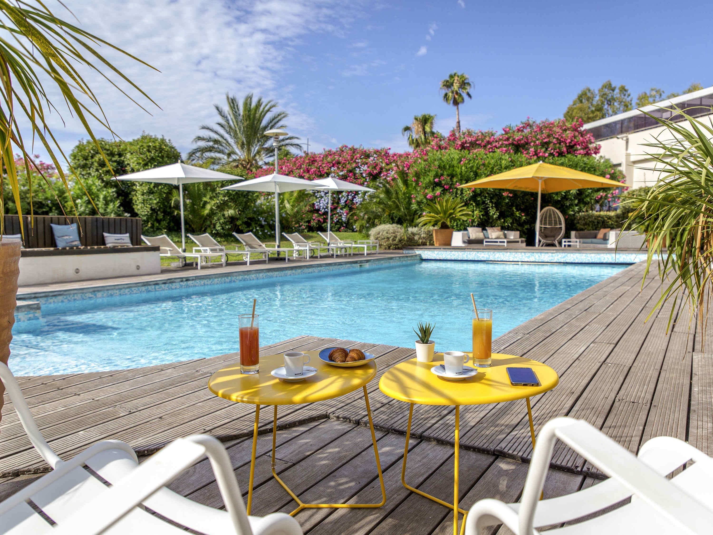 Zona de piscina con sillones reclinables, sombrillas y una mesa con bebidas y una pequeña planta.