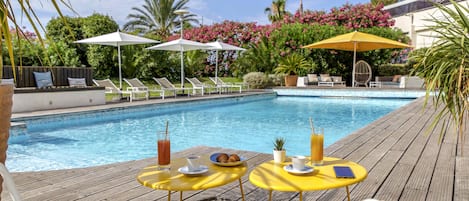 Zona de piscina con sillones reclinables, sombrillas y una mesa con bebidas y una pequeña planta.