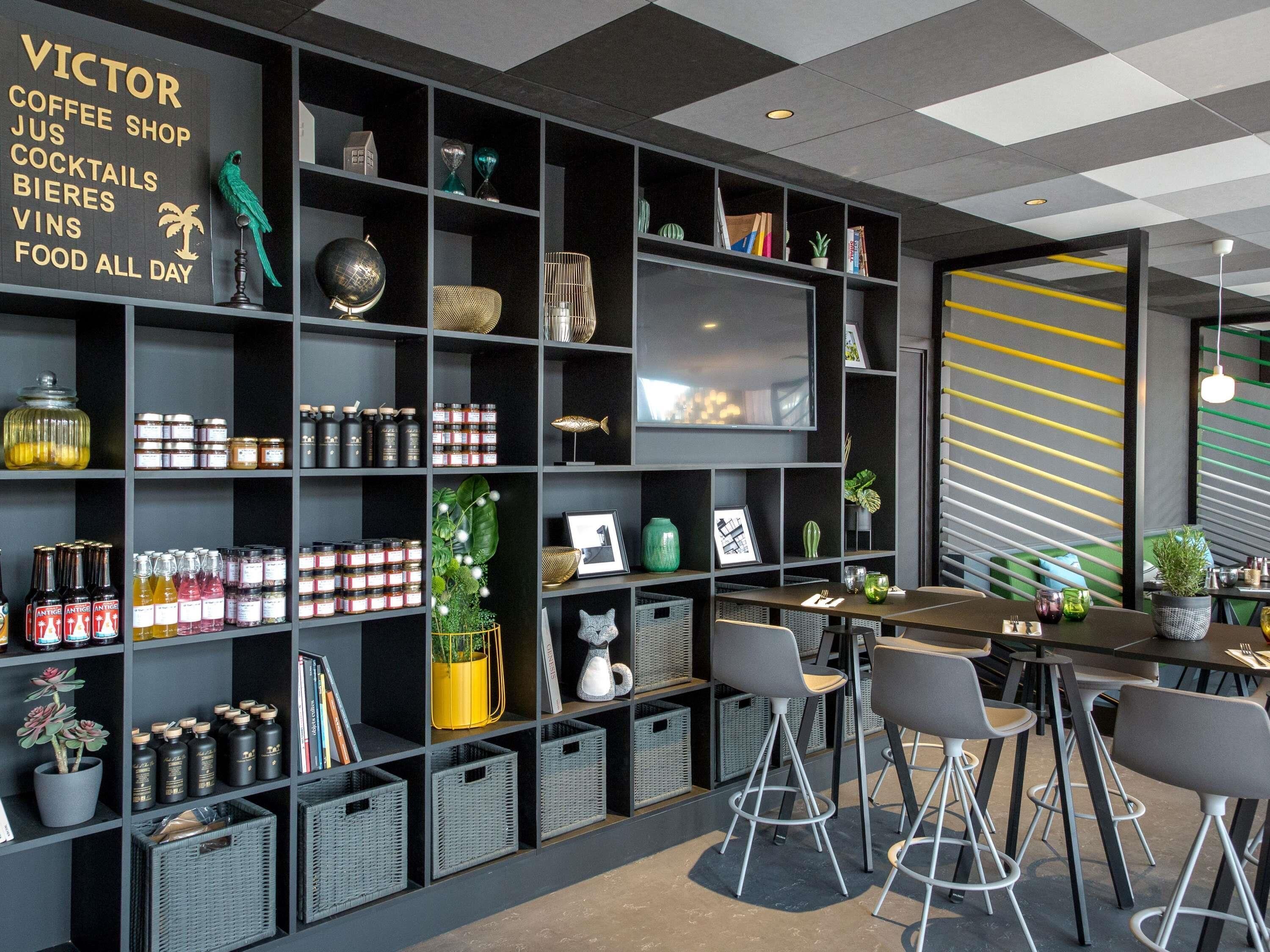 Een modern interieur met een bord van een koffiebar, planken met diverse artikelen, en een zithoek met barstoelen.