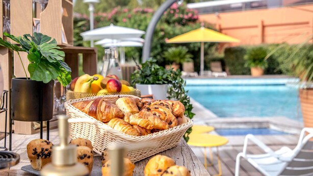 A poolside buffet with bread, pastries, and fruits.