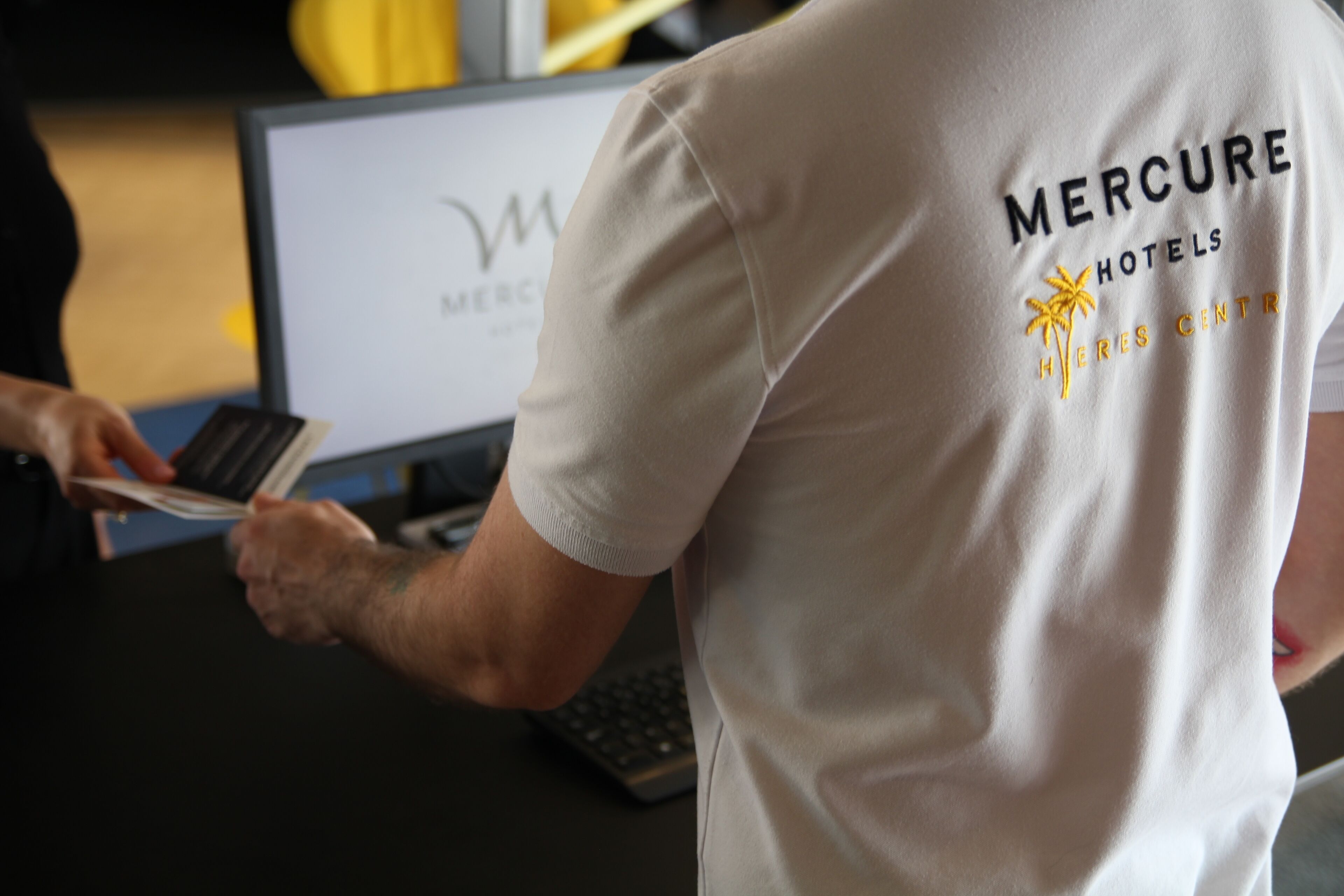 Una persona con una camisa de Mercure Hotels, manejando una tarjeta en un escritorio con una computadora portátil y un teclado.