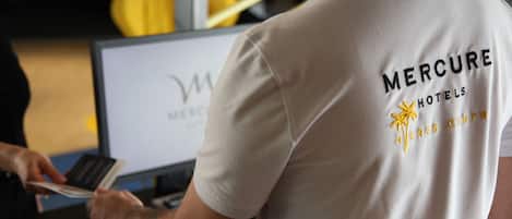 Una persona con una camisa de Mercure Hotels, manejando una tarjeta en un escritorio con una computadora portátil y un teclado.