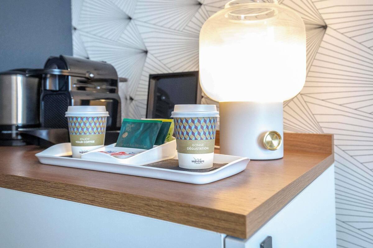A kitchen counter with a coffee station, including a tray with coffee cups and a pack of coffee pods, and a modern light fixture.