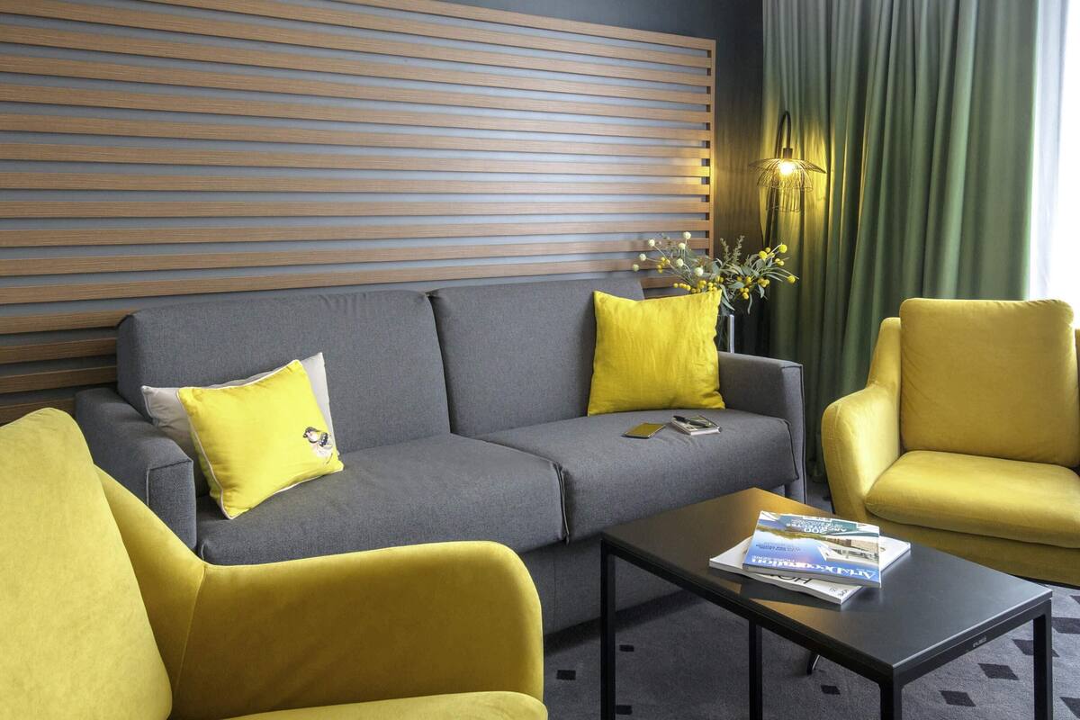 Una sala de estar moderna con un sofá gris, sillones amarillos, una mesa de centro negra y una pared de listones de madera.